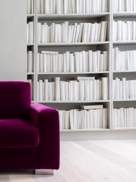 A deep claret chair at the end of pale shelves.